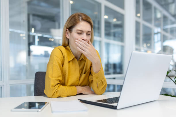 istock Sleepy young woman yawning while working on laptop in modern office 2163075523