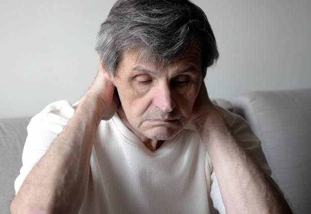 An elderly man with a severe migraine massages his gray head at home after work.