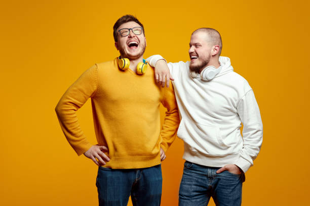 istock Two men with headphones smiling while having fun in studio, standing isolated over yellow background 2163079730