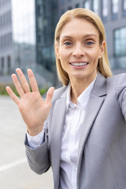 istock Professional woman waving and smiling while on a video call outside office building 2163080457