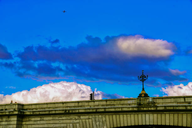 Putney Bridge, London, UK. July 20, 2024. Summer, white clouds and a bright, clear blue sky, White fluffy clouds; the River Thames, the riverside in the London Borough of Wandsworth. The composition is framed to highlight the bridge's design, lines and curves against the expansive sky.