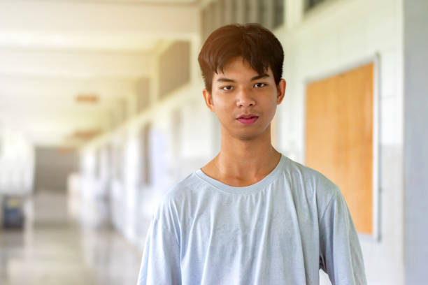 Asian schoolboy standing in front of the door of his classroom in normal shirt when he goes to school on weedend, soft focus.
