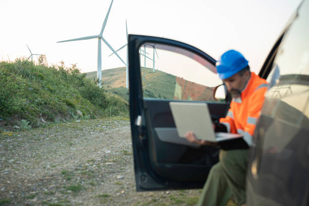 Eco energy concepts. Man with car checking wind turbines with AI software on laptop. Carbon neutrality and sustainable energy.