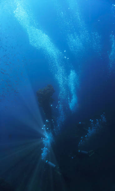 istock Scuba divers in blue dreamlike environment at a wreck 2163108755