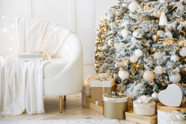 istock Cozy holiday room with white sofa draped in blanket, Christmas tree decorated with lights and ornaments, gold and white gift boxes, festive ambiance 2163112954
