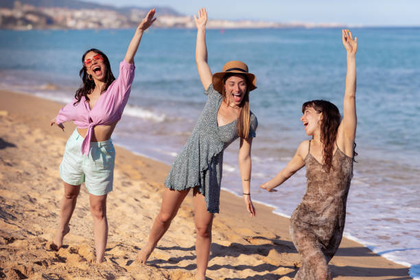 istock Three friends on the beach with arms raised having fun looking at camera 2163116392