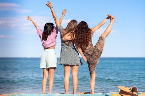 istock Three friends on the beach with arms raised having fun looking at camera 2163116868