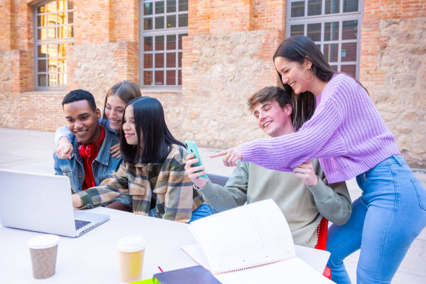 A group of students with laptops sit near the campus and communicate.