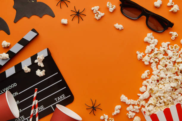 istock Popcorn, clapperboard, paper cup and halloween decor on a red background. Flat lay, copy space. 2163132268