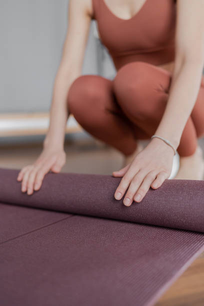istock Woman trainer rolling out a mat after class. Rolled yoga mats in a studio create a peaceful atmosphere for meditation and exercise. 2163141004