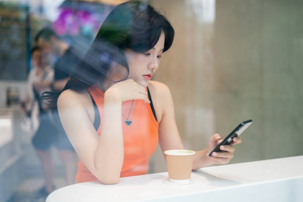 istock Young Asian Woman Using Phone by Cafe Window Relaxingly 2163161773