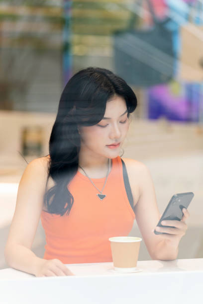 istock Young Asian Woman Using Phone by Cafe Window Relaxingly 2163161839