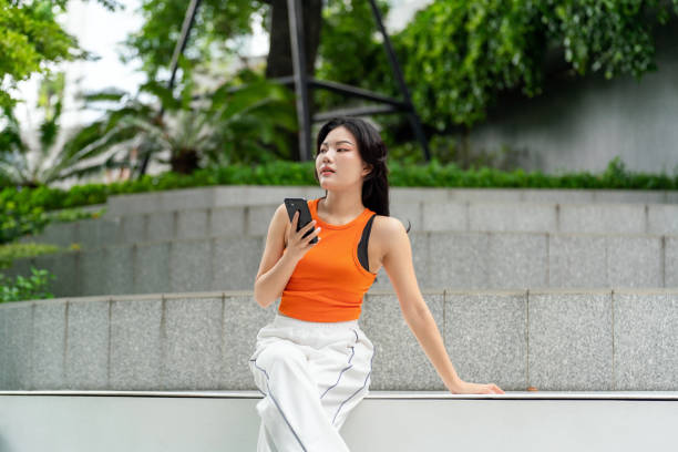 istock Young Asian Woman Looking Away While Using Phone in Park 2163162015