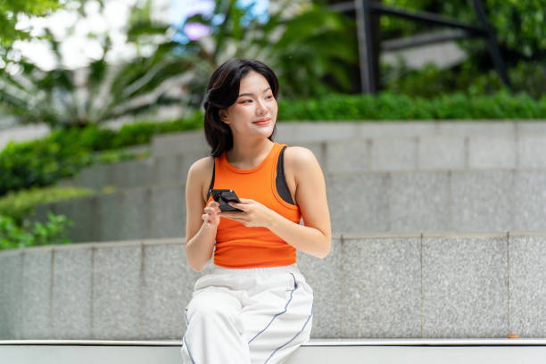 Young Asian Woman Looking Away Smiling While Using Phone in Park