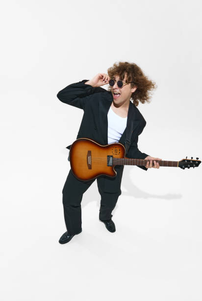 istock Musician in sunglasses and a suit, young man playing guitar, making creative performance isolated on white background 2163165496