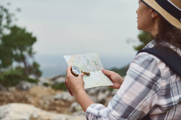 istock Woman with a backpack and hat exploring nature with a map and compass in hand on a hiking trip 2163166785