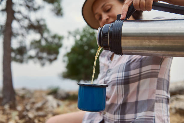 istock Woman pouring hot tea from a thermos into a blue camping cup outdoors in a forest setting 2163166855