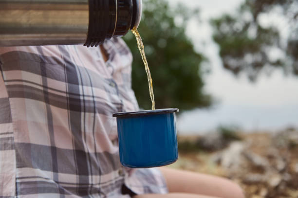 istock Person pouring hot beverage from thermos into blue mug outdoors in a serene nature setting 2163166880