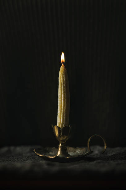 corn in a candlestick instead of a candle. the corn looks like a candle. Dark background