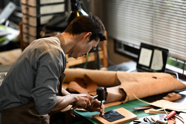 istock Focused artisan holding a tool and a hammer to puncture or shape leather on a workbench 2163167416