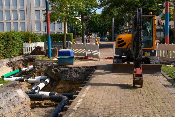 Large pipes for installation, construction site with trench and excavator.