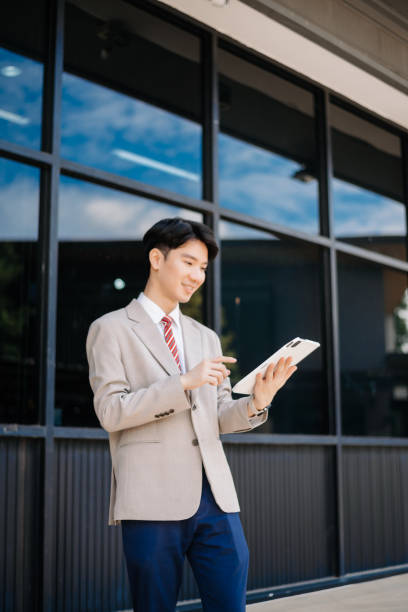 istock Confident Asian man with a smile standing holding notepad and tablet at out side office. big city on business center 2163168728