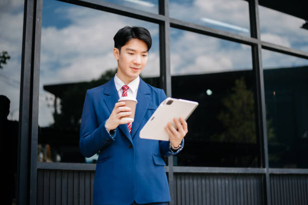 istock Confident Asian man with a smile standing holding notepad and tablet at out side office. big city on business center 2163168733