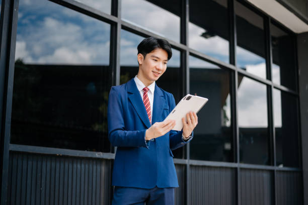 istock Confident Asian man with a smile standing holding notepad and tablet at out side office. big city on business center 2163168737