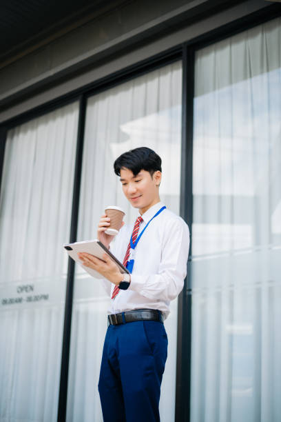 istock Confident Asian man with a smile standing holding notepad and tablet at out side office. big city on business center 2163168738