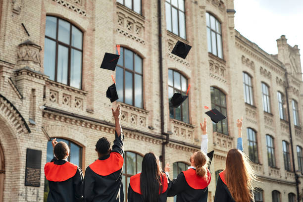 Graduates joyfully celebrating outside university building after academic achievement A group of graduates in academic attire rejoice in their achievement by throwing caps in the air outside a historic university building, celebrating success and the culmination of their education graduation throwing cap stock pictures, royalty-free photos & images
