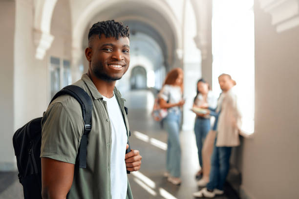 istock A student with a smile is walking in a university hallway as classmates chat in the background 2163169774