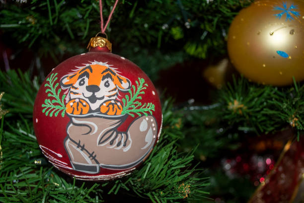 A red ball with a tiger cub in a boot on the festive tree. Christmas tree toy. Festive Christmas tree decoration