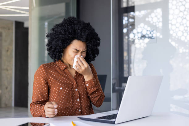 istock Young woman sneezing while working at her office desk 2163175923