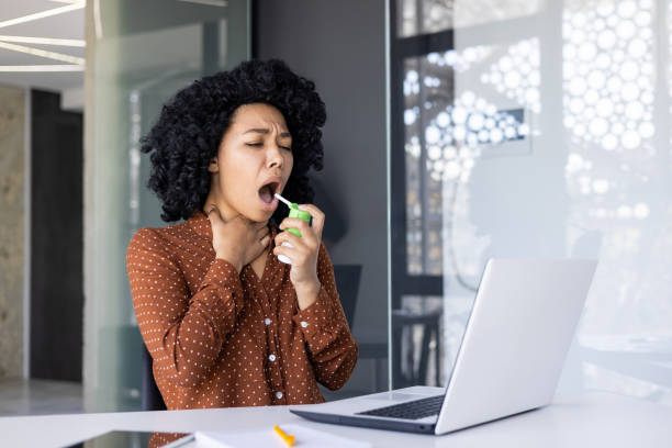 istock Young woman using throat spray in modern office setting 2163178635