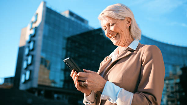 istock Smiling Senior Businesswoman Using Smartphone Outdoors in Modern Urban Setting 2163179695