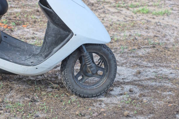 part of one grey scooter with black wheel stands on the ground on the street