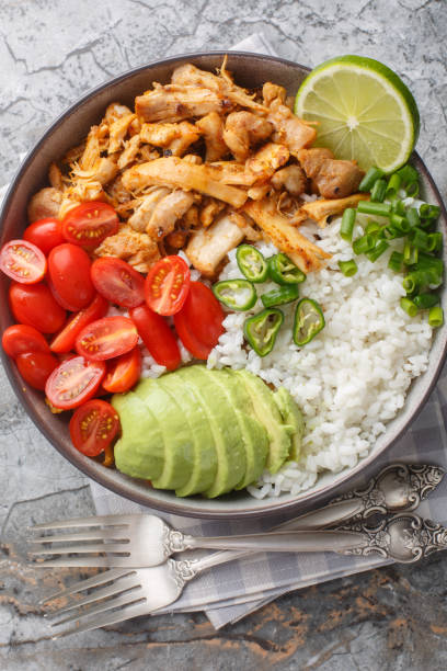 istock Bowl with pulled spicy chicken, rice, cherry tomatoes, avocado, jalapano pepper close-up on the table. Vertical top view 2163190703