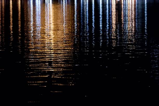 istock Blurred colorful light reflection on river surface with water waves in the dark night background 2163196576