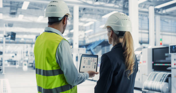 istock Caucasian Male Process Engineer Using Tablet And Talking To Female Supervisor At Autonomous Assembly Line At Modern Electronics Factory. Colleagues Wearing Hardhats, Discussing New Complex Projects. 2163197550
