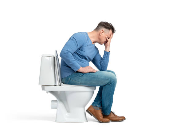 istock A dressed man sits on the toilet, cupping his face with his palm, facepalming. Side view. Isolated on a white background. 2163205497