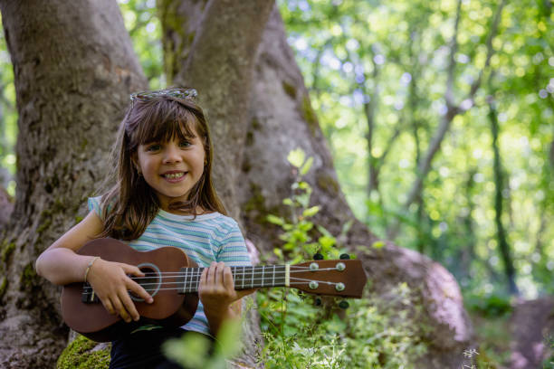 Portrait of smiling little girl looking at camera and playing ukulele.