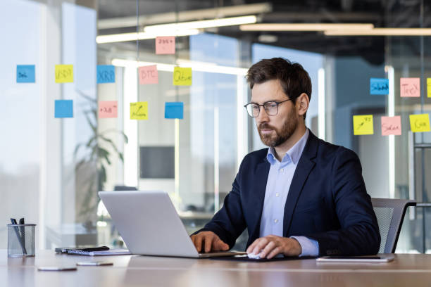 istock Business professional working on laptop in modern office with sticky notes on glass wall 2163207213