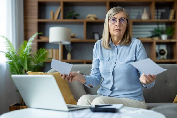 istock Stressed senior woman holding bills while using laptop at home 2163207391