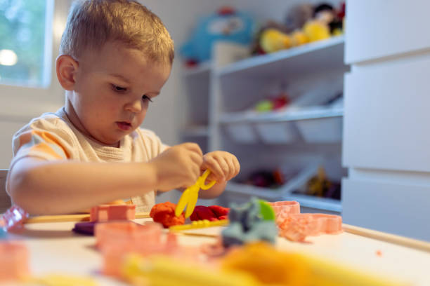 istock Focused boy with colorful plasticine sculpturing figure at table in room 2163208292