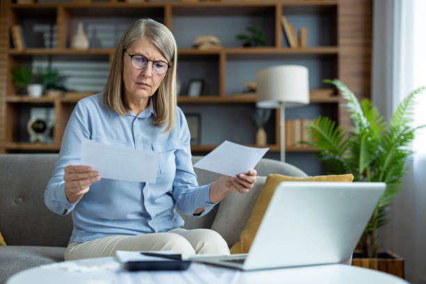 istock Senior woman reviewing documents at home while using a laptop, feeling focused and concerned 2163208350