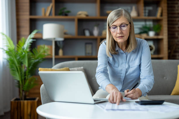istock Mature woman working on laptop at home pointing at documents on table 2163209276