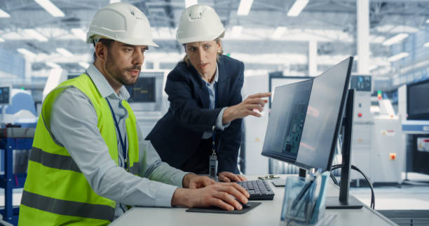 istock Electronics Research and Development Facility: Caucasian Female Manager Consults Male Engineer. Professionals Wear Hardhats And Design Microchips And Semiconductors On Computer At The Factory. 2163210313