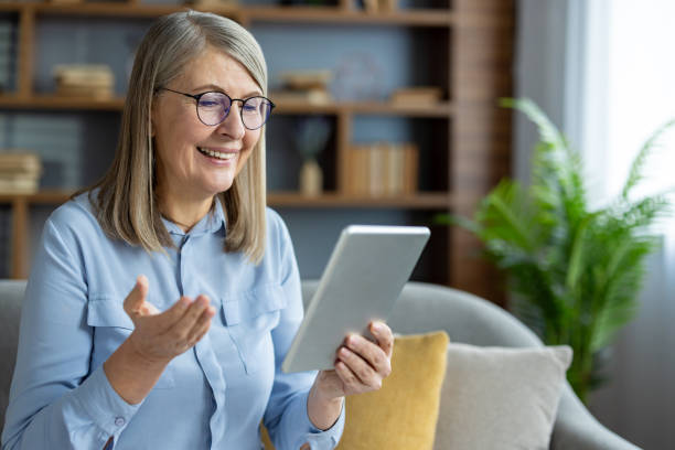 istock Smiling senior woman using tablet for video call at home 2163210540