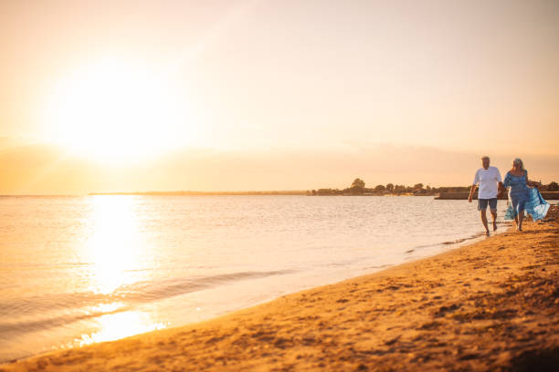istock Couple walking on beach at sunset, holding hands calmly. 2163215415