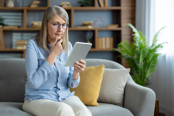 istock Senior woman using tablet on sofa at home, browsing internet or reading 2163217518